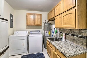 A compact kitchen with wooden cabinets, a granite countertop, a built-in sink, and a washer-dryer unit. - Coos Bay Farmhouse Near Ocean, Pet-Friendly (Coos Bay)