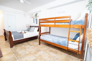 A room with two wooden bunk beds, a door, a small table with a plant, and a wall-mounted shelf with decorative items. - Azul Beach Apartments, Apt. 1: A Cozy Apartment Just Steps from the Beach… (Boquerón)