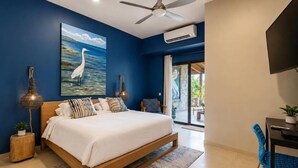 A bedroom with a bed, a ceiling fan, an air conditioning unit, a painting of a bird, and a view of the outdoors.