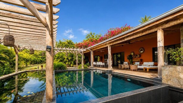 A pool area with a wooden pergola, outdoor seating, and a stone wall.