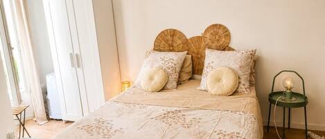 A bedroom with a bed, a wardrobe, a bedside table with a lamp, and a small stool.