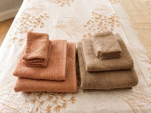 Two sets of folded towels on a bed with a floral pattern. - Elegant and cozy studio apartment in the historic center of Hyères (Hyères)