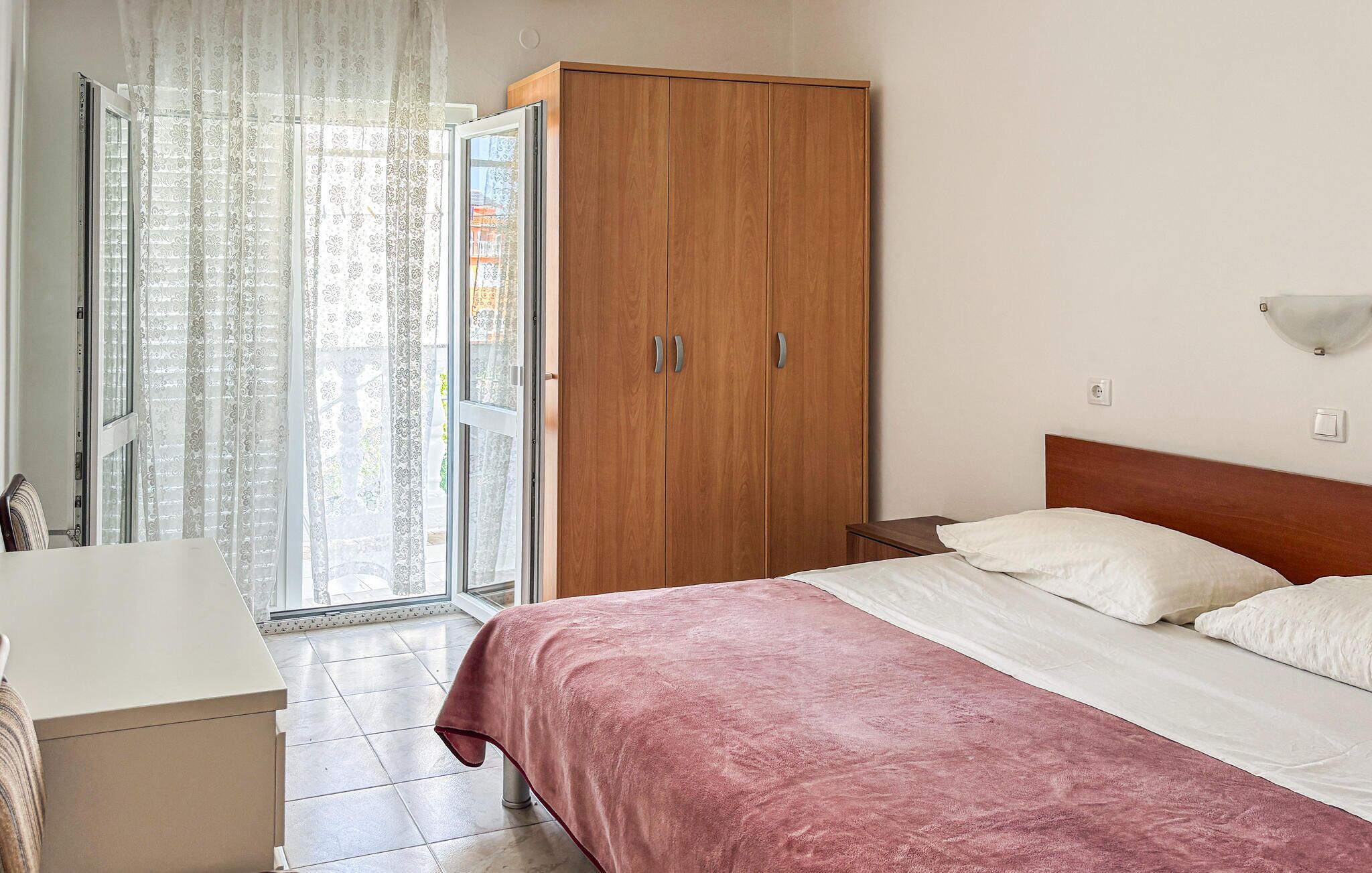 A bedroom with a bed, a wooden wardrobe, a bedside table, and a window with curtains.