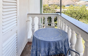 Ein Balkon mit rundem Tisch, der mit einer blauen Tischdecke bedeckt ist, weißes Geländer und Blick auf eine natürliche Landschaft.