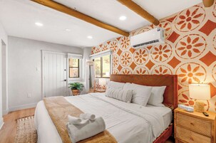Una habitación de hotel con cama, mesita de noche, lámpara y aire acondicionado de pared.