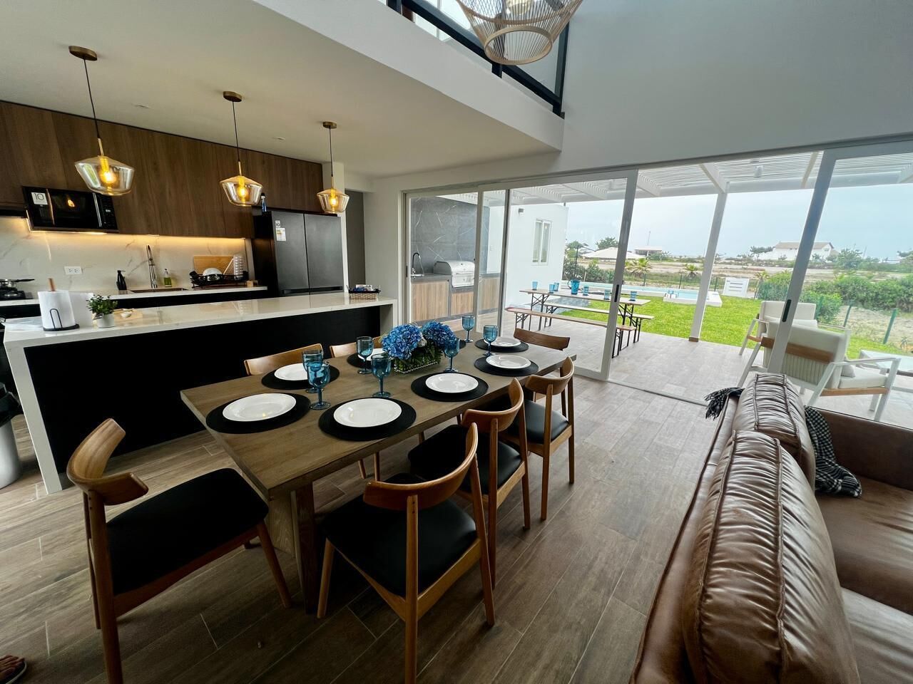 A modern kitchen with a dining area, large windows, and a view of the outdoors.