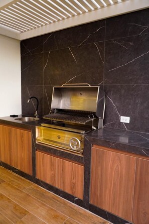 A modern kitchen with a built-in grill, wooden cabinets, and a marble backsplash.
