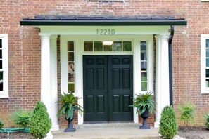 A brick building with a dark green double door, white columns, and the number 12210 above the entrance.