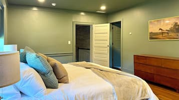 A bedroom with a bed, a nightstand, a lamp, a door, and a painting on the wall.