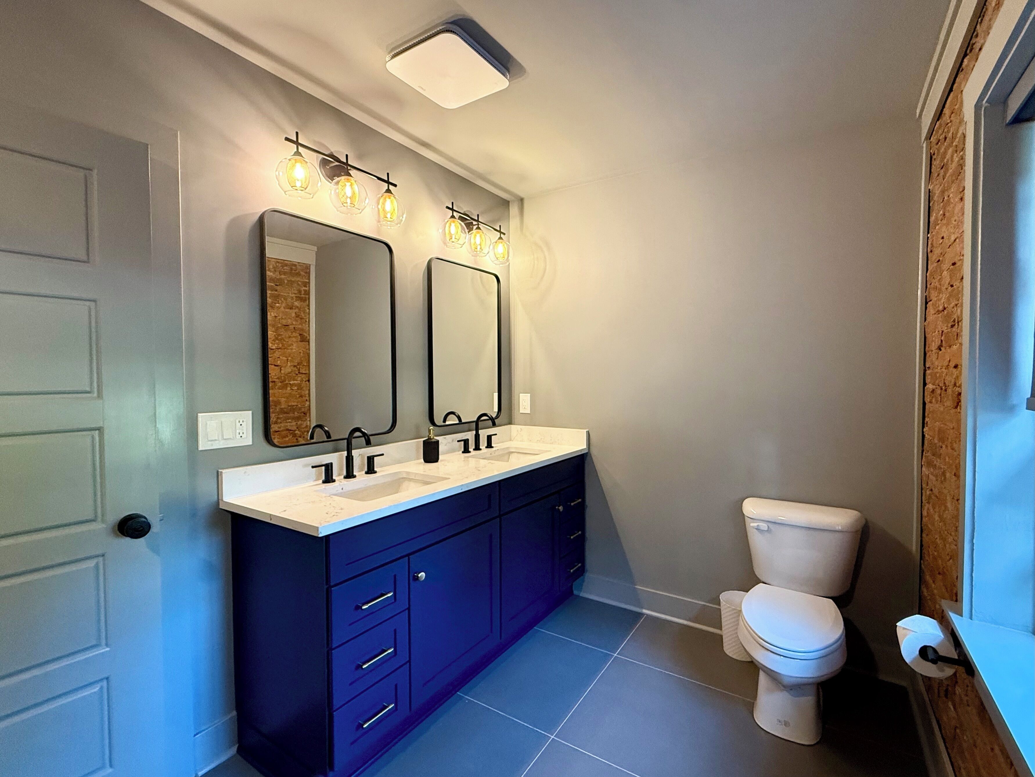 Un bagno moderno con un mobile lavabo doppio, due specchi fissati alla parete, un water e un lampadario sopra gli specchi.