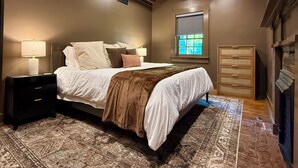 Quarto com cama, mesas de cabeceira, janela e lareira.