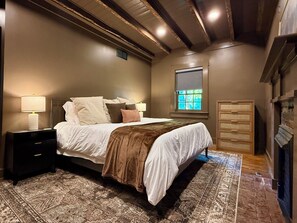 Un dormitorio con cama, mesitas de noche, una ventana y una chimenea.
