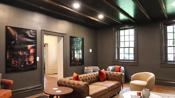 Uma área de estar moderna com um sofá de couro marrom, poltronas bege e uma mesa de centro redonda. Há obras de arte emolduradas nas paredes e uma grande janela que proporciona luz natural.
