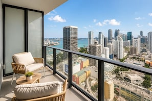 A balcony with wicker furniture and a view of a cityscape with high-rise buildings and a body of water.