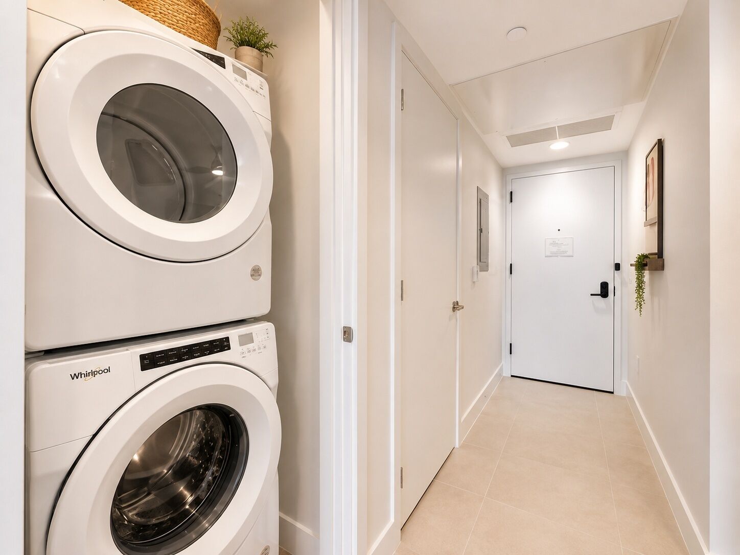 A laundry area with stacked washers and dryers, a hallway with doors, and a wall-mounted plant.