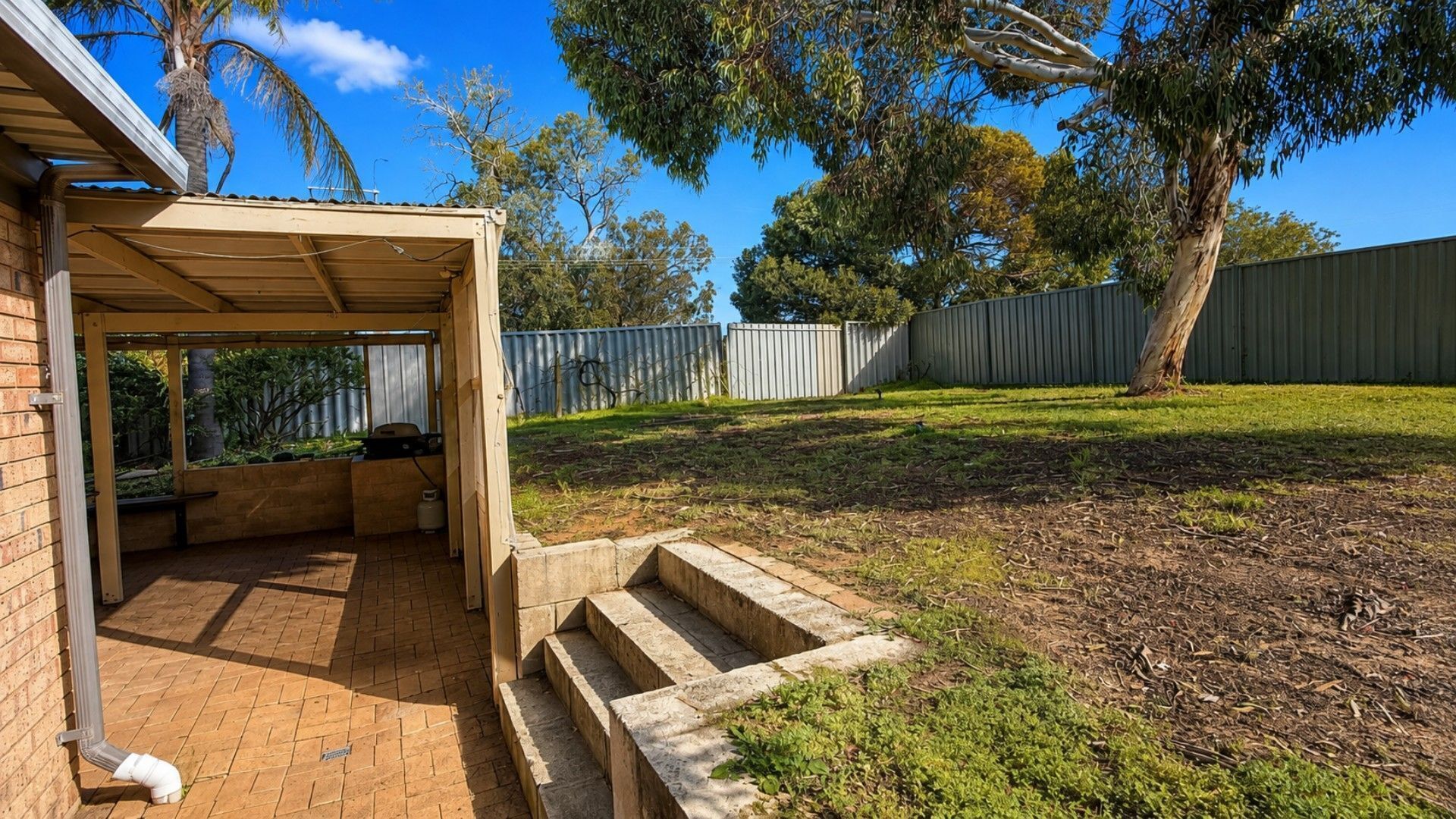 Un espace extérieur abrité avec un barbecue, des marches menant à une terrasse et une cour clôturée.