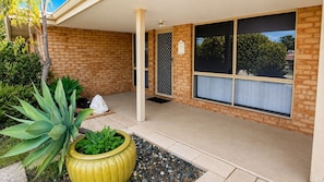 A covered outdoor area with a brick wall, large windows, and potted plants.
