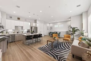 A modern kitchen with white cabinets, a central island with bar stools, a dining area with a table and chairs, and a living room with a sofa and a zebra-patterned rug. - Cozy Northside home ~20 mins to downtown Houston (Houston)