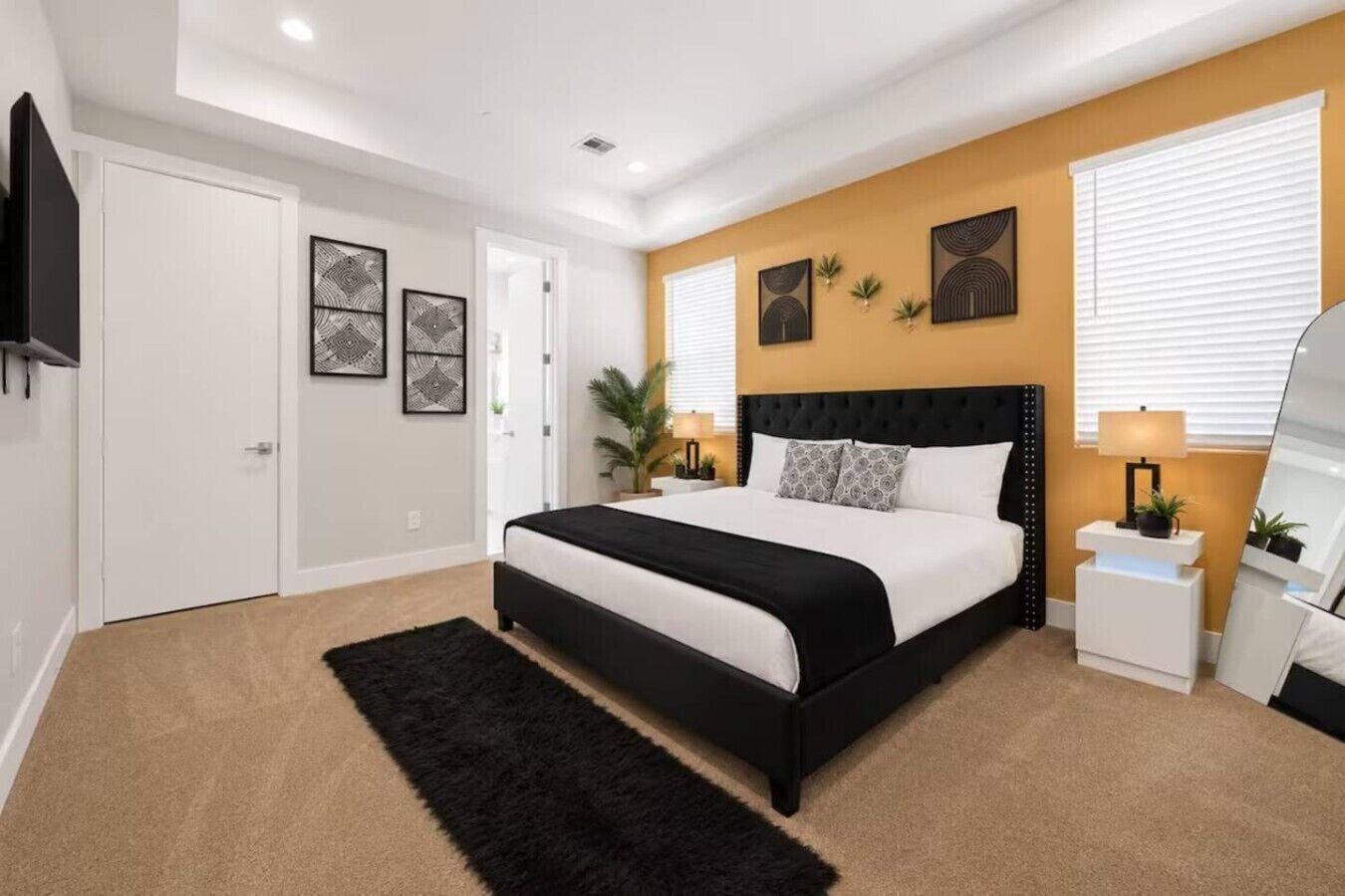 Quarto moderno com cama preta e branca, tapete preto e mesa de cabeceira branca com abajur.