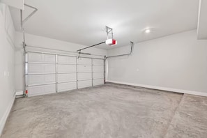Eine Garage mit weißen Garagentüren, einer an der Decke befestigten Lampe und einem Betonboden.