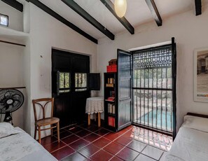 A room with a bed, a chair, a fan, a bookshelf, and a door leading to an outdoor area. - Fantastic 6-bedroom house in Nocaima perfect for group getaways (Nocaima)