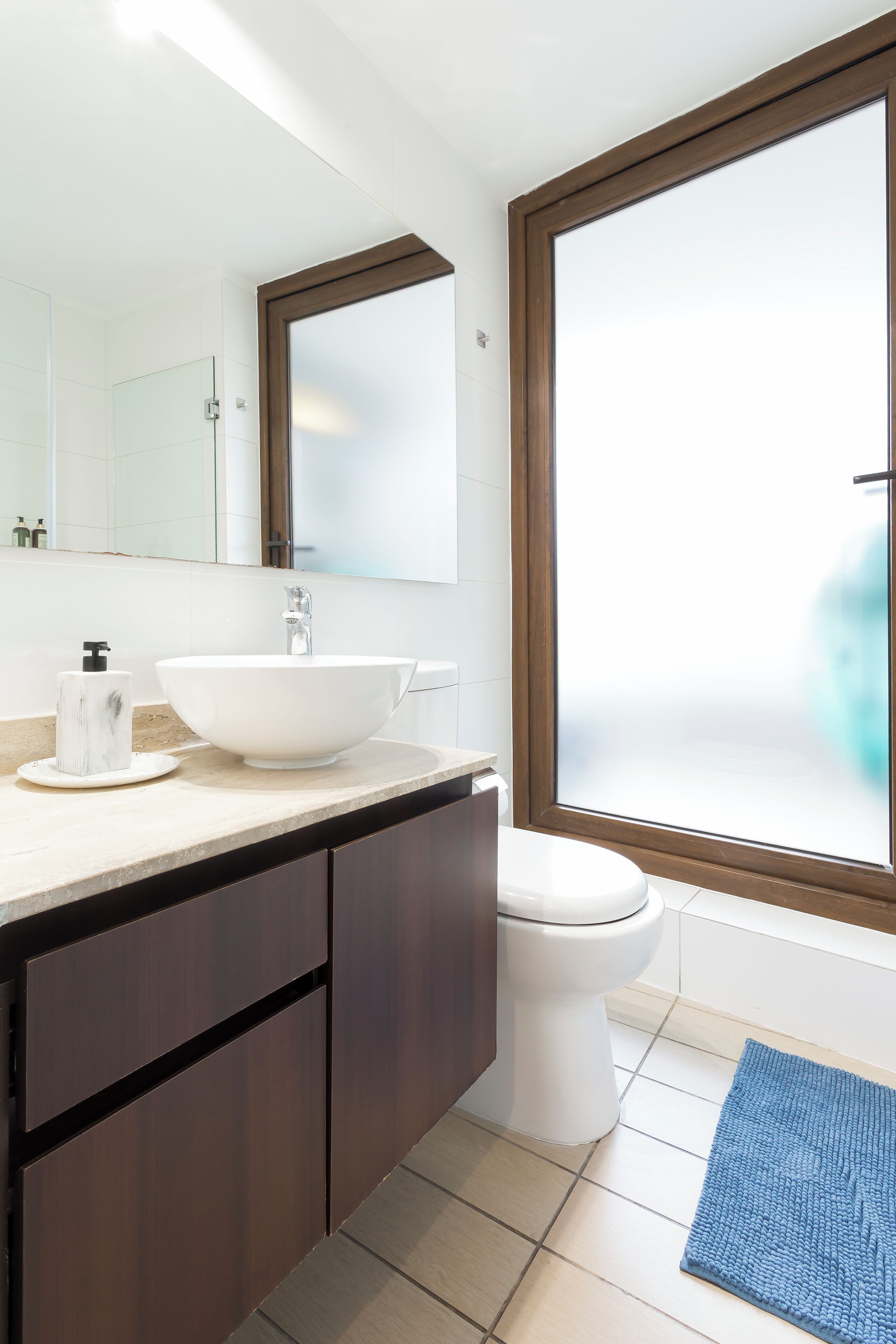 Ein modernes Badezimmer mit einem großen, weißen Waschbecken, dunklen Holzschränken, einer Toilette und einem Fenster mit Milchglas.