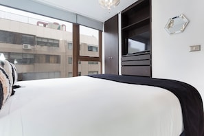 A bedroom with a bed, a wardrobe, a television, and a view of a building outside. - Excellent Location in Las Condes | Just Steps from the Manquehue Metro Station (Las Condes)