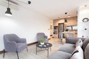 A modern living room with grey sofas, a round table with a plant, and a kitchen in the background. - Excellent Location in Las Condes | Just Steps from the Manquehue Metro Station (Las Condes)