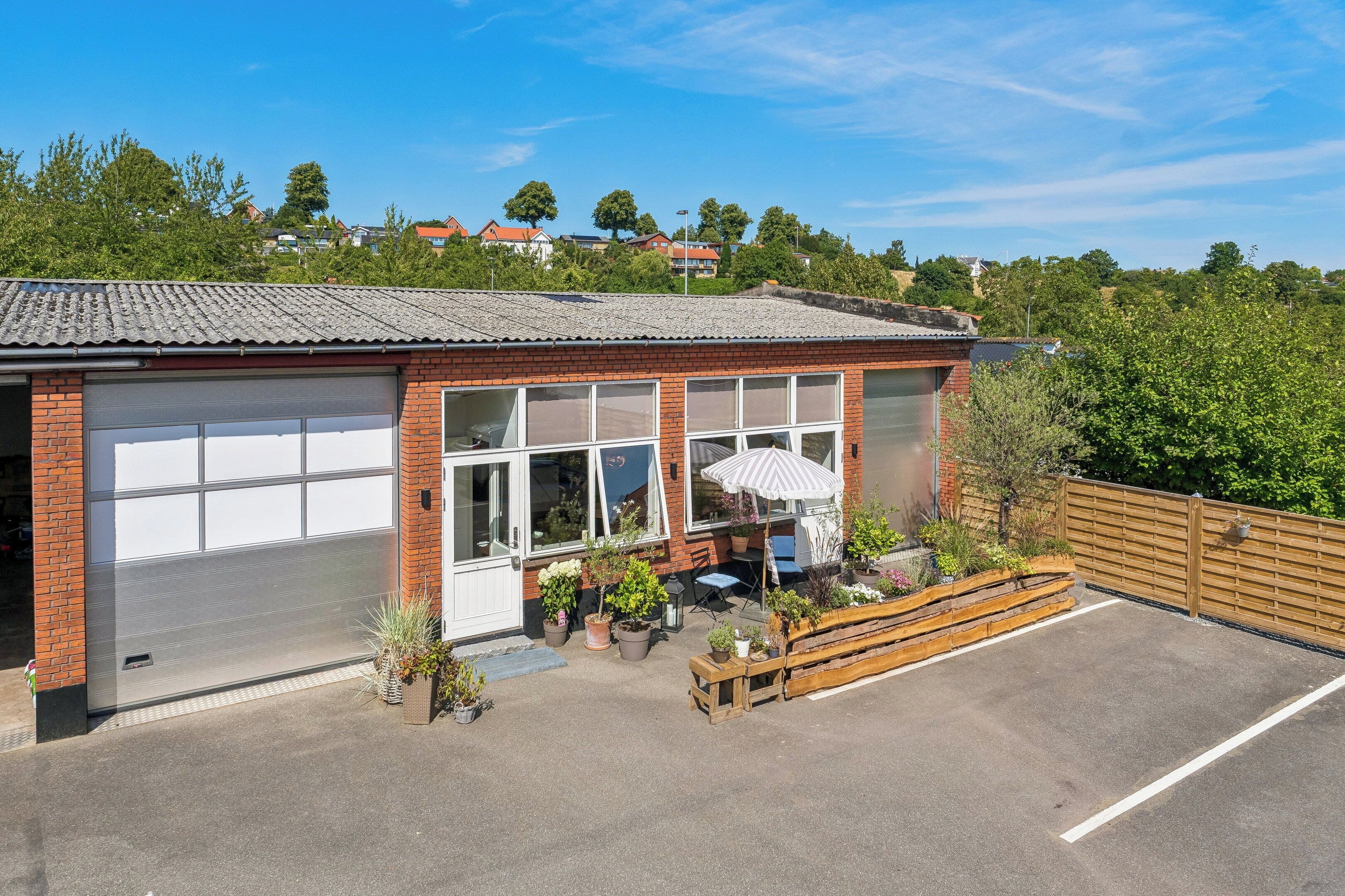 En etagers bygning med garage, terrasse med siddepladser og udsigt over et boligområde.