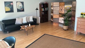 Una sala de estar con un sofá negro, una mesa de centro, una estantería y un panel decorativo en la pared.