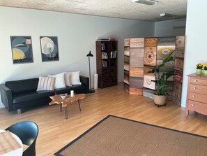 A living room with a black sofa, a coffee table, a bookshelf, and a decorative wall panel. - Cozy apartment with Bali-inspired terrace (Svendborg)