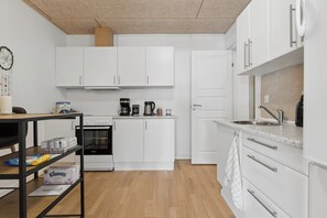A modern kitchen with white cabinets, a stainless steel sink, and a coffee maker. - Cozy apartment with Bali-inspired terrace (Svendborg)