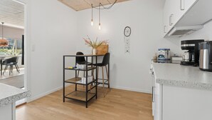 Una cocina compacta con piso de madera, una mesa con estructura de metal y sillas, una cafetera y un atrapasueños en la pared.