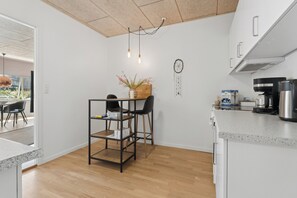 A compact kitchen with a wooden floor, a metal-framed table with chairs, a coffee machine, and a dreamcatcher on the wall. - Cozy apartment with Bali-inspired terrace (Svendborg)
