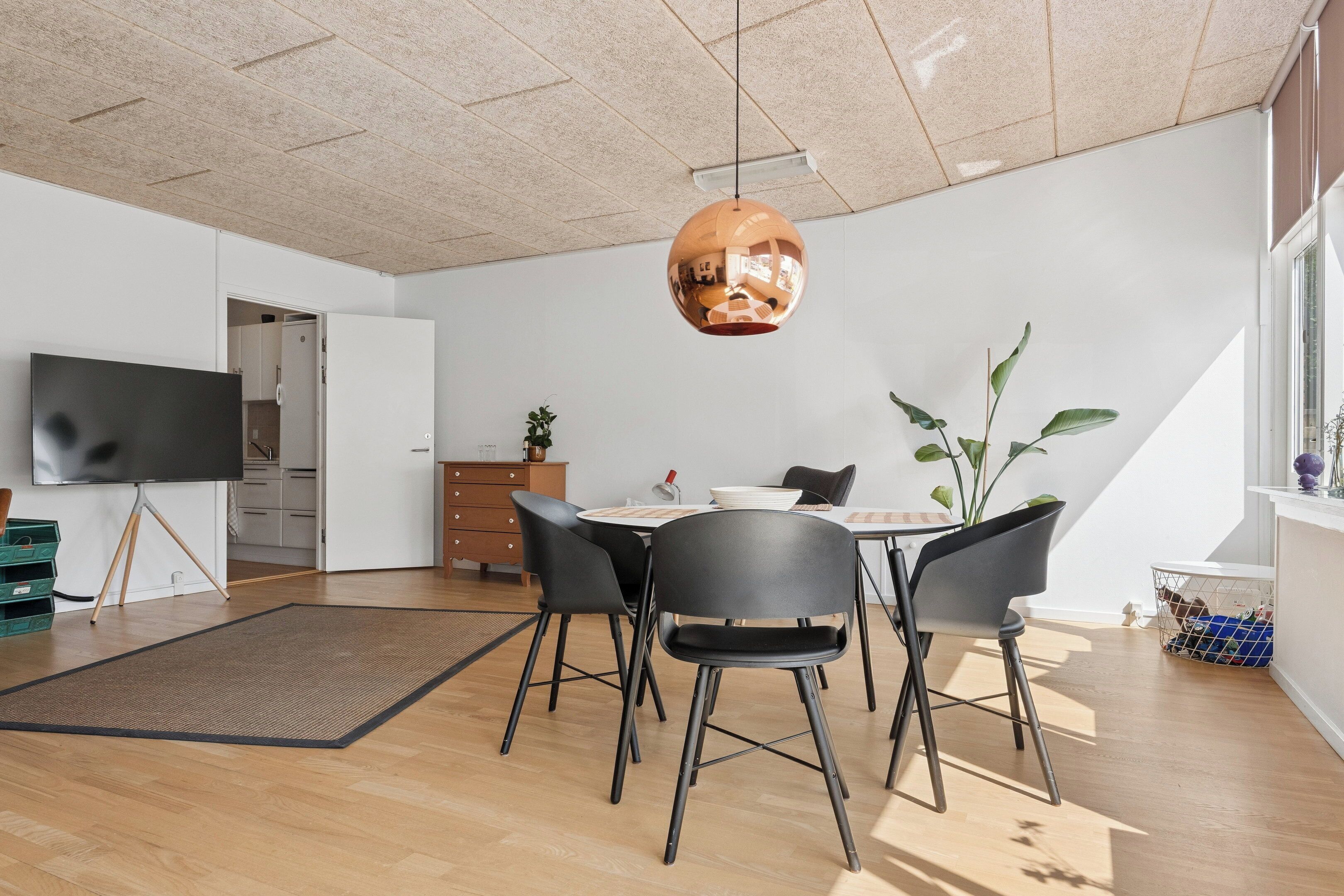 Et moderne spiseområde med et rundt bord, sorte stole og en hængende lampe.