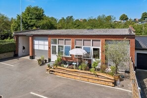 A small building with a garage door, a wooden bench, and potted plants. - Cozy apartment with Bali-inspired terrace (Svendborg)
