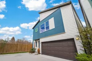 A two-story residential building with a garage, a small front porch, and a clear sky. - Sleek New Retreat in Up-and-Coming Houston (Houston)
