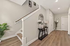 A hallway with a staircase, a console table with a vase, and a potted plant. - Sleek New Retreat in Up-and-Coming Houston (Houston)