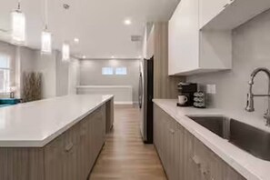 A modern kitchen with a central island, stainless steel appliances, and pendant lighting. - Sleek New Retreat in Up-and-Coming Houston (Houston)
