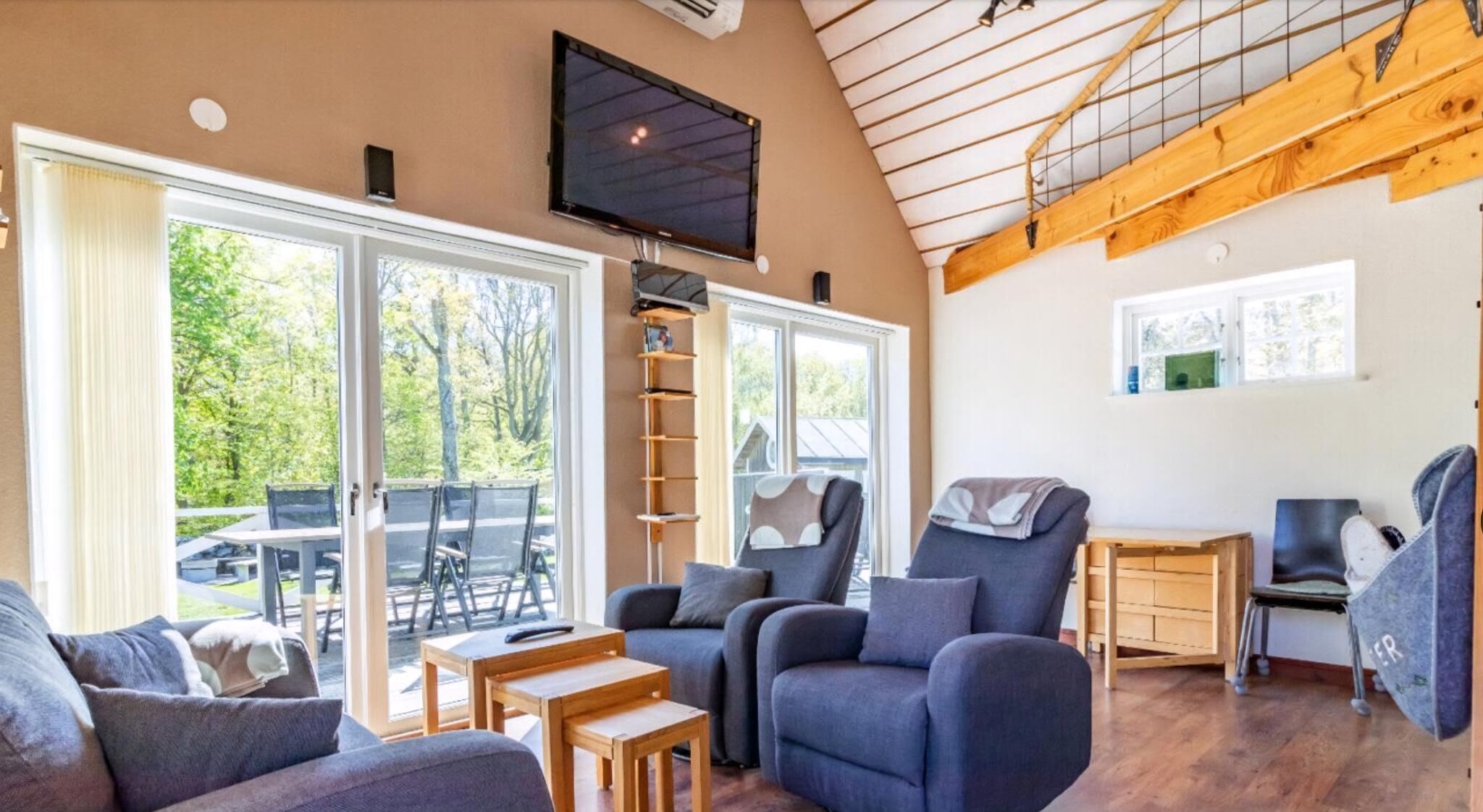 A spacious living area with a high ceiling, large windows, and a TV mounted on the wall.