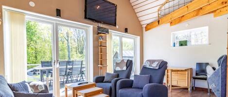 A spacious living area with a high ceiling, large windows, and a TV mounted on the wall.
