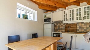 Eine kleine Küche mit Holztisch, Schränken, einer Mikrowelle, einem Kühlschrank und einem Fenster.