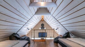 Ein quadratisches Schlafzimmer im Dachgeschoss mit Holzbalken an der Decke, Holzdielenboden und zwei Betten mit Kissen.