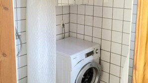 Eine kompakte, weiße Waschmaschine in einem kleinen Waschraum mit gefliesten Wänden und einer Holztür.