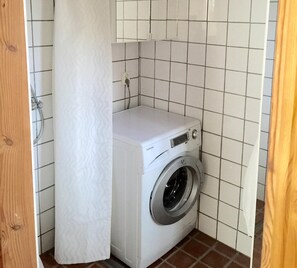 A compact, white washing machine in a small laundry room with tiled walls and a wooden door. - Holiday home on the beautiful island of Aspö (Drottningskär)
