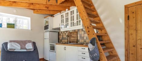 A compact kitchen with white cabinets, a built-in oven, and a wooden staircase.