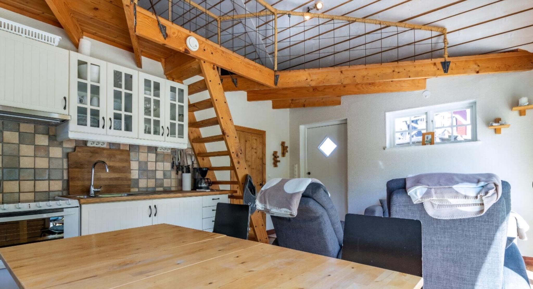 A kitchen with wooden beams, a dining table, and a staircase.