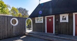 A wooden building with a red door, a small window, and a circular window. - Holiday home on the beautiful island of Aspö (Drottningskär)