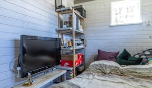 Une chambre à coucher avec un lit, une télévision, une étagère remplie de livres et une lampe, ainsi qu’une fenêtre ornée d’œuvres d’art.
