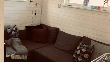 A cozy corner with a brown sofa, two patterned pillows, a throw blanket, and a window with a shelf above it.